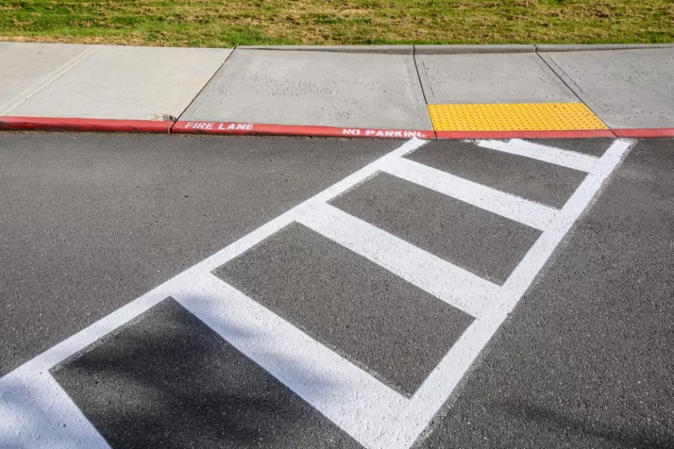 Freshly painted white crosswalk leading to yellow curb cut to sidewalk